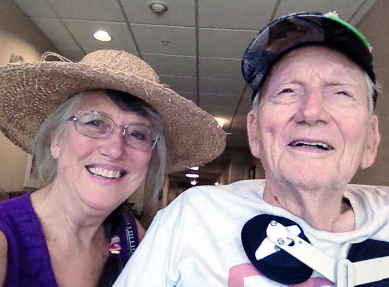 A woman with her father, Housecall Providers patient, smiling inside of a building while wearing hat